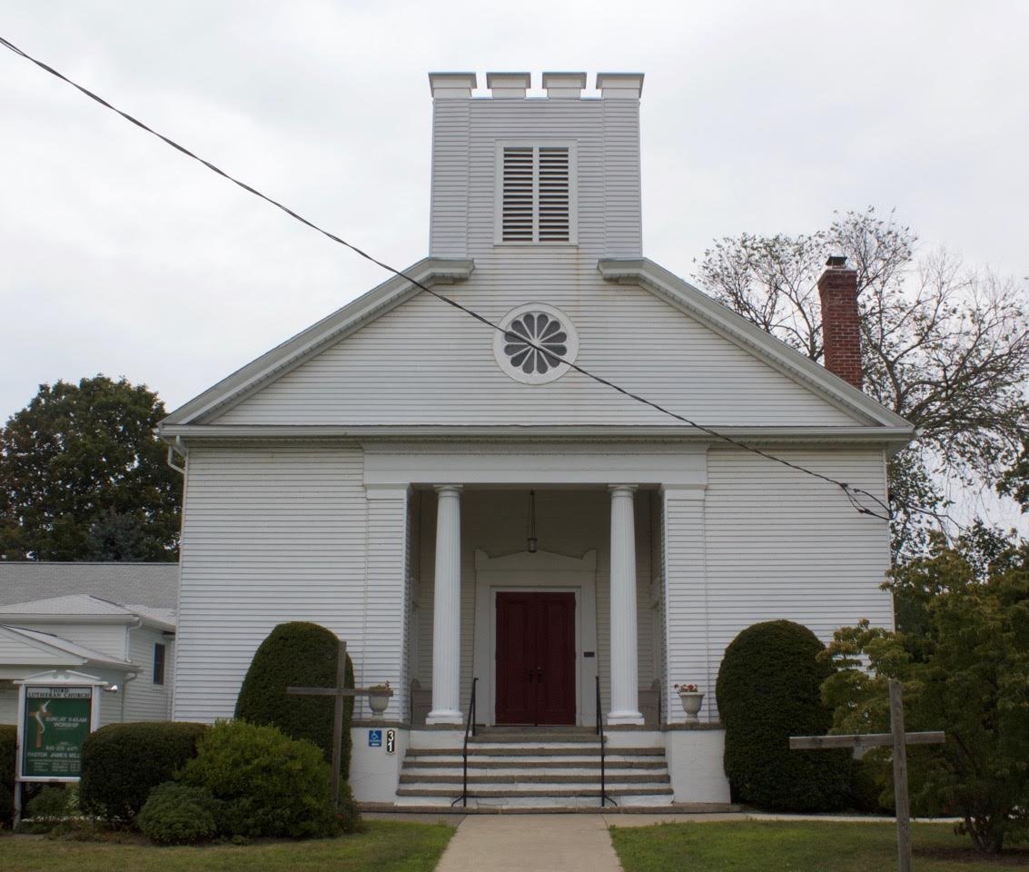 Front view of a white church building with columns and a steeple, surrounded by trees and shrubs. Rhinebeck NY Porchfest