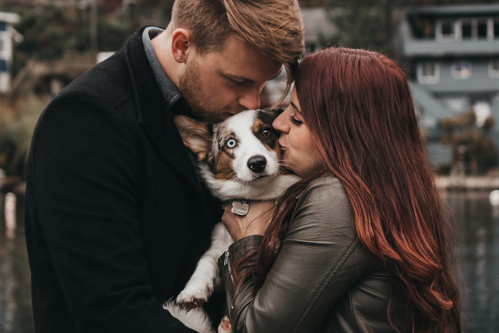 A couple hugging and kissing a dog with one blue eye.