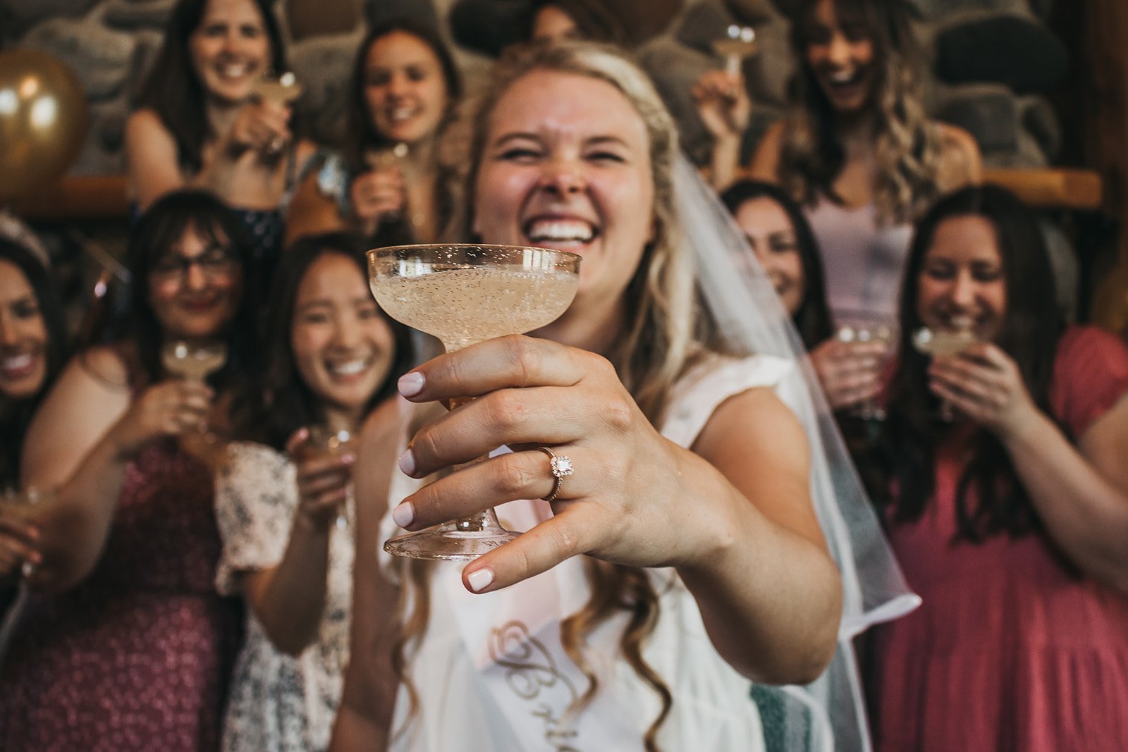 Bride and friends celebrating with champagne glasses in hand, smiling and laughing together.