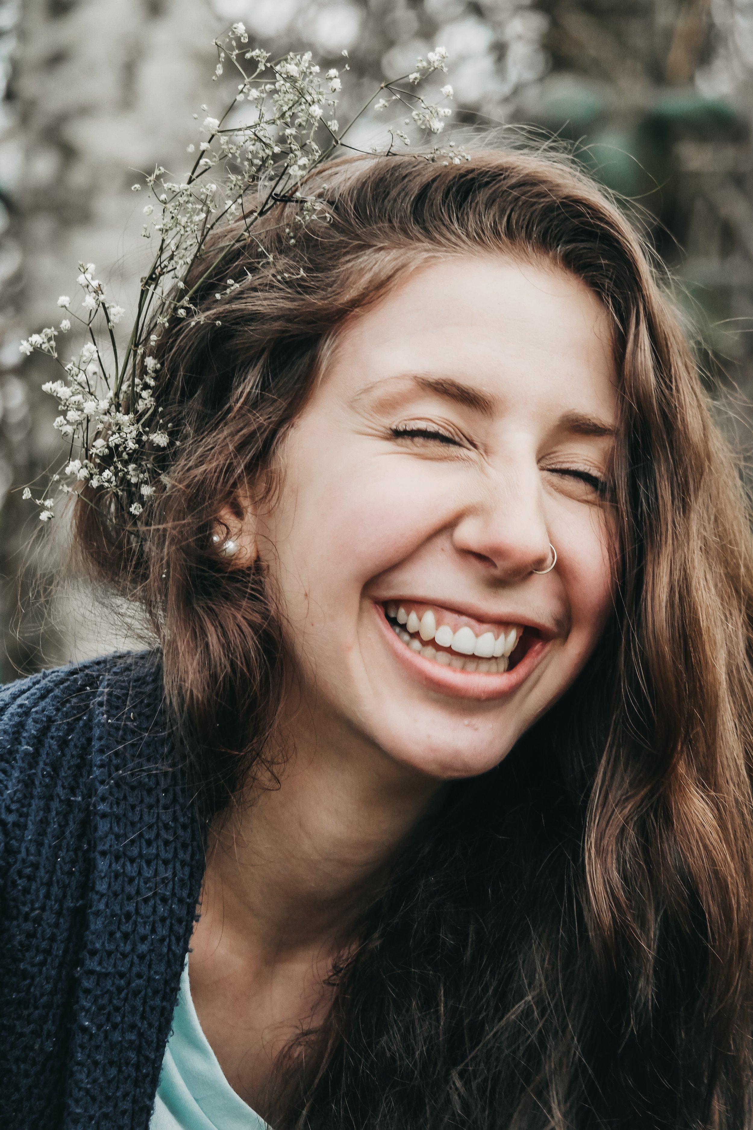 Woman smiling, wearing a blue sweater, with flowers in her hair.