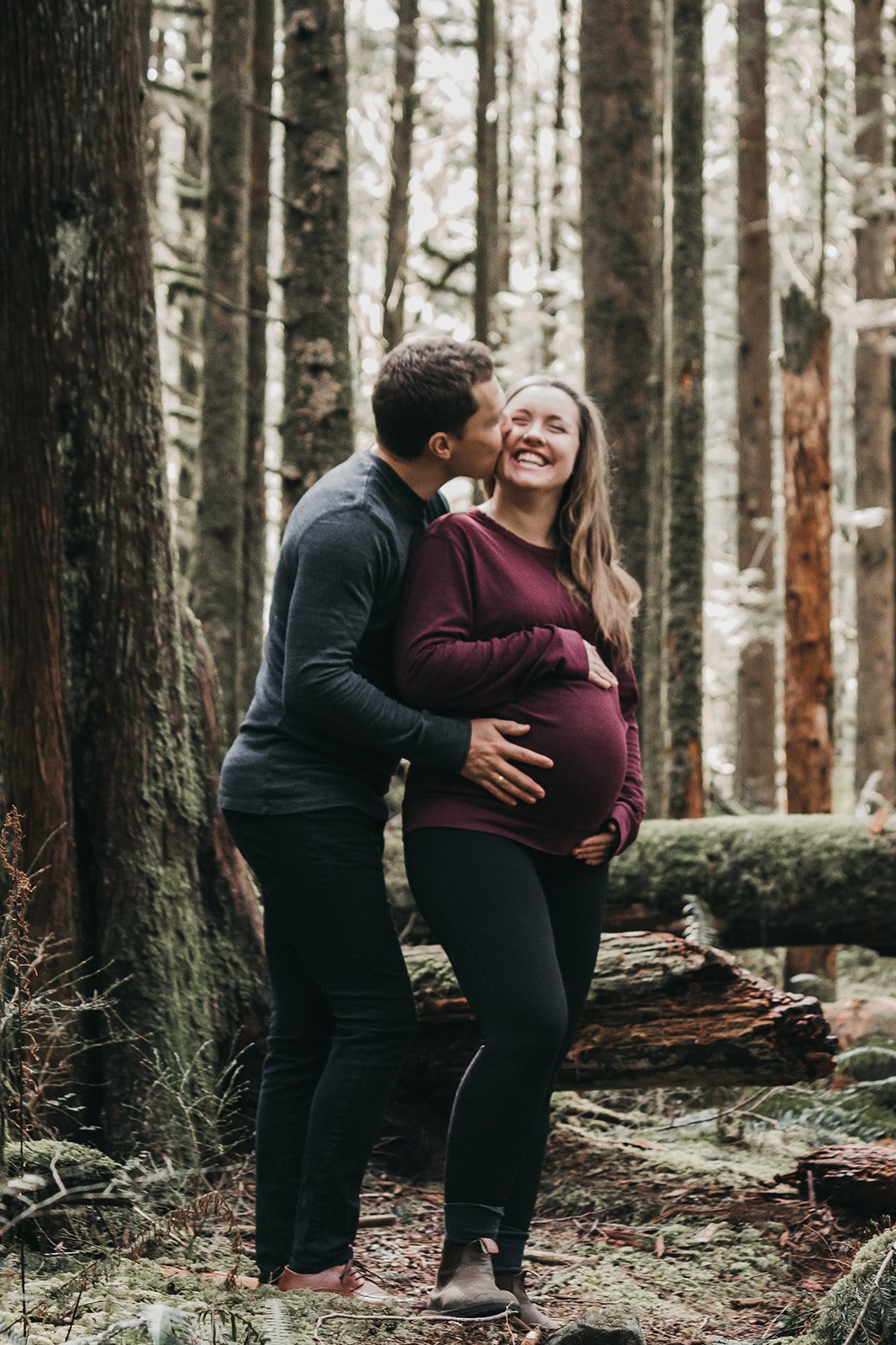 Pregnant couple embracing and smiling in a forest setting