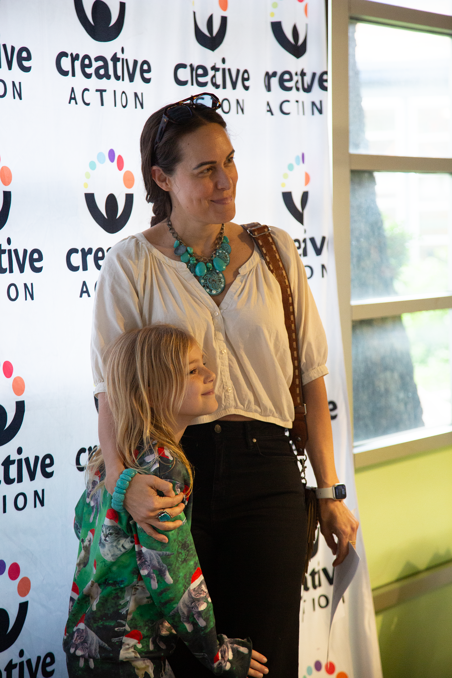A woman and young girl pose in front of a Creative Action backdrop during an after school showcase.