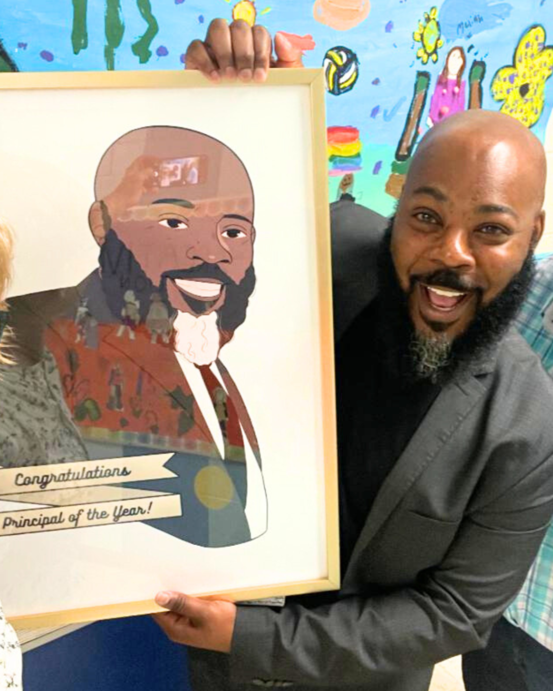Man holding a colorful framed illustration of himself, smiling, with celebratory message 'Congratulations Principal of the Year!' while standing in front of a vibrant, decorated background.