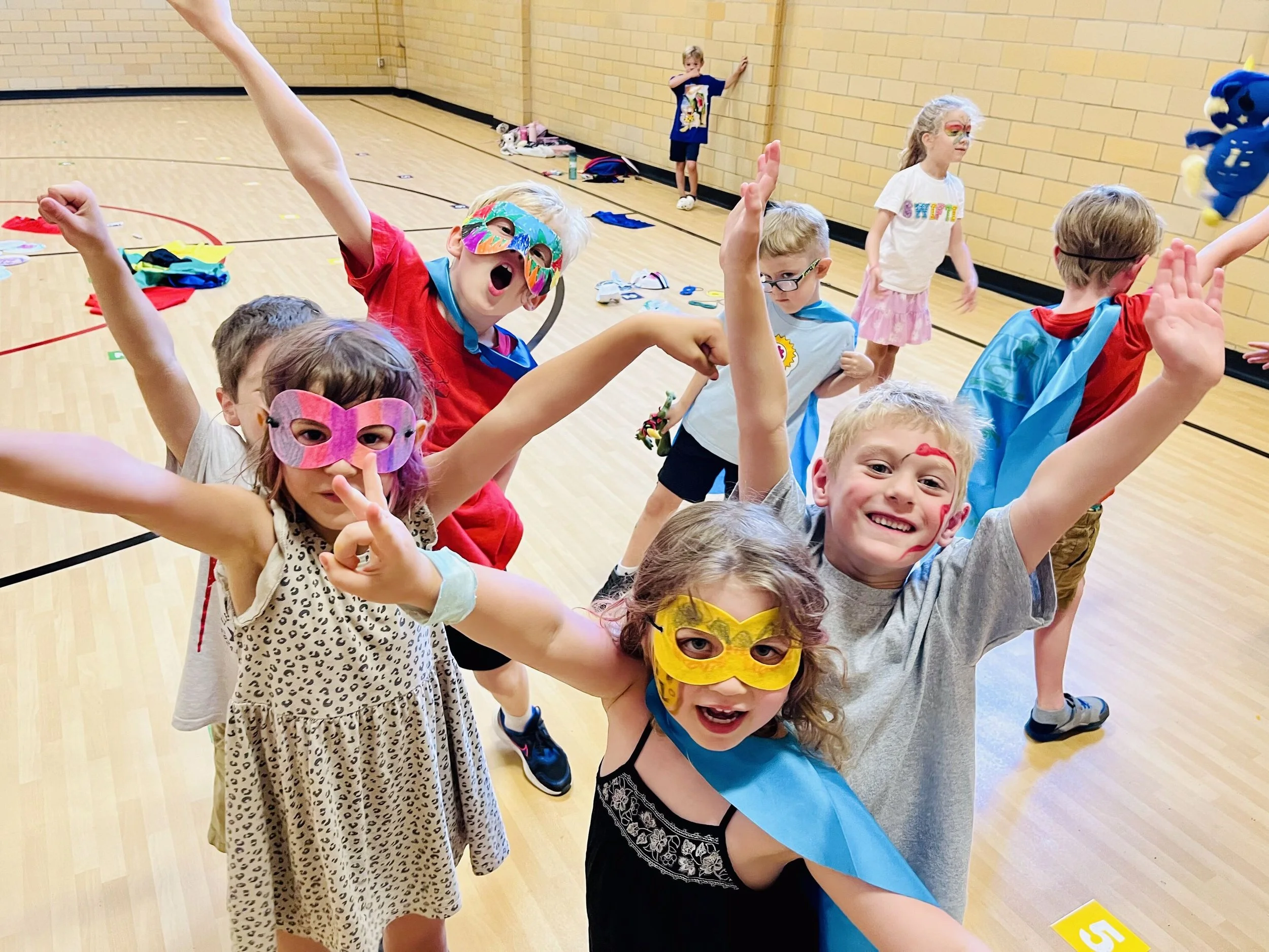 Children wearing colorful masks and costumes playing in gymnasium.