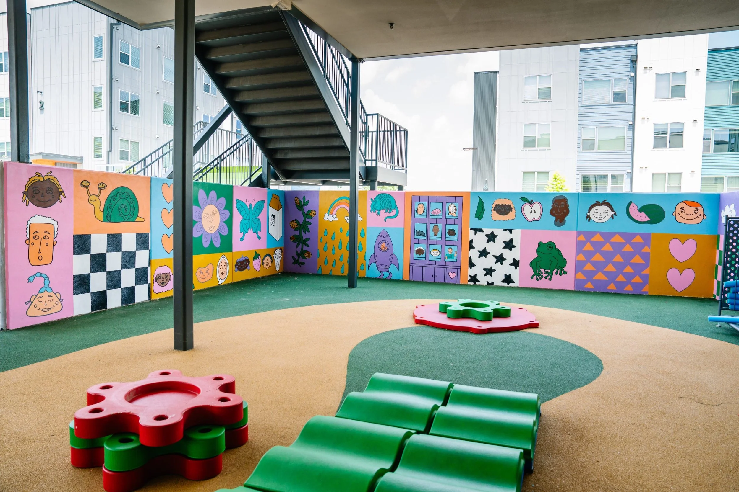 Colorful outdoor play area with painted wall, small trees, and a staircase, situated in an urban apartment complex.