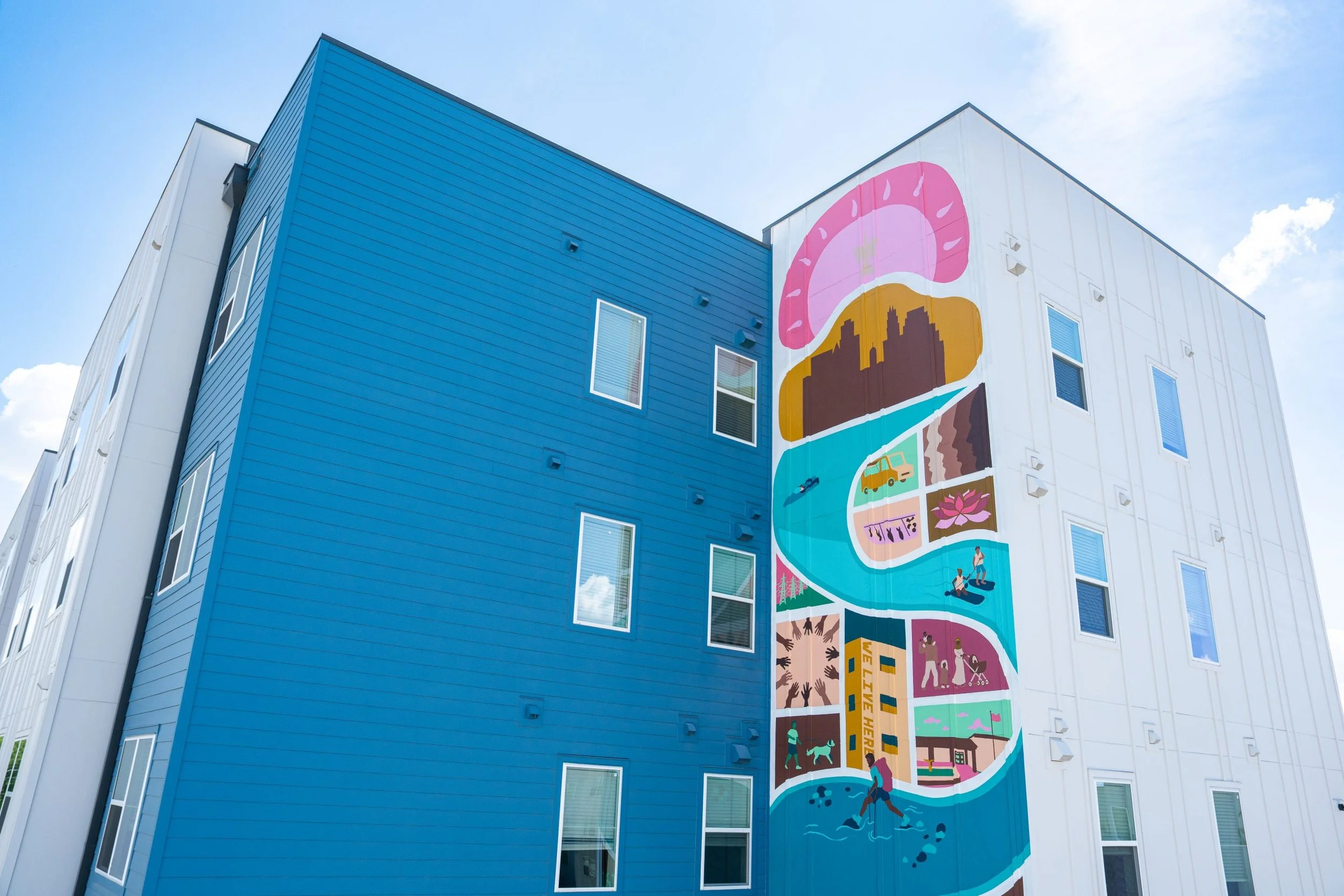 Colorful mural on the side of a multi-story building depicting various community and outdoor activities such as walking, gardening, and playing sports against a blue sky with some clouds.