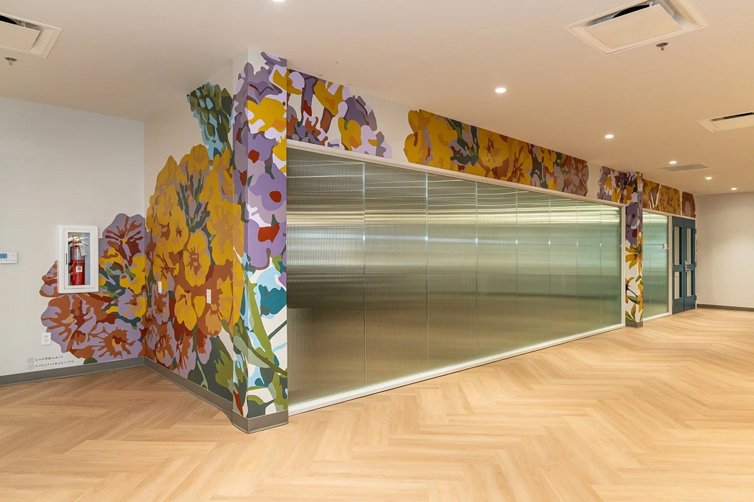 Interior of a modern building with floral mural on walls, wooden flooring, and frosted glass partitions.