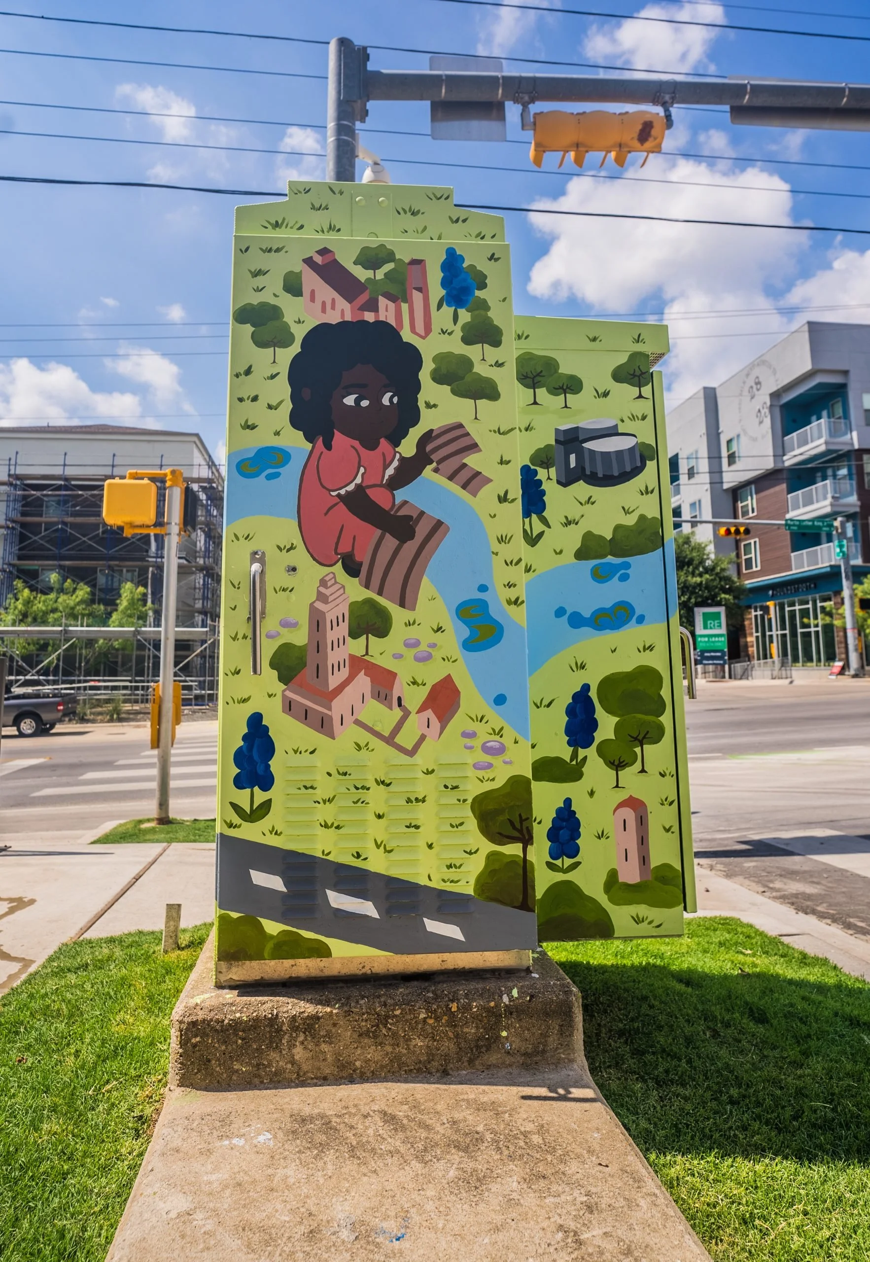 Colorful mural depicting a woman with dark skin and curly black hair sitting by a stream, surrounded by trees, buildings, and a church tower, with a blue sky and clouds overhead.