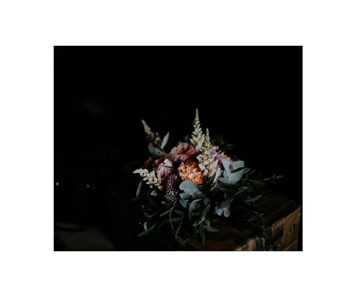 A bouquet of pink and peach flowers with green and gray foliage on a wooden surface against a black background.