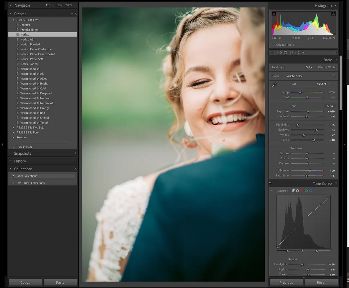 A woman with blonde hair smiling and winking, wearing white earrings, outdoors with a green background, close-up shot taken during daylight.