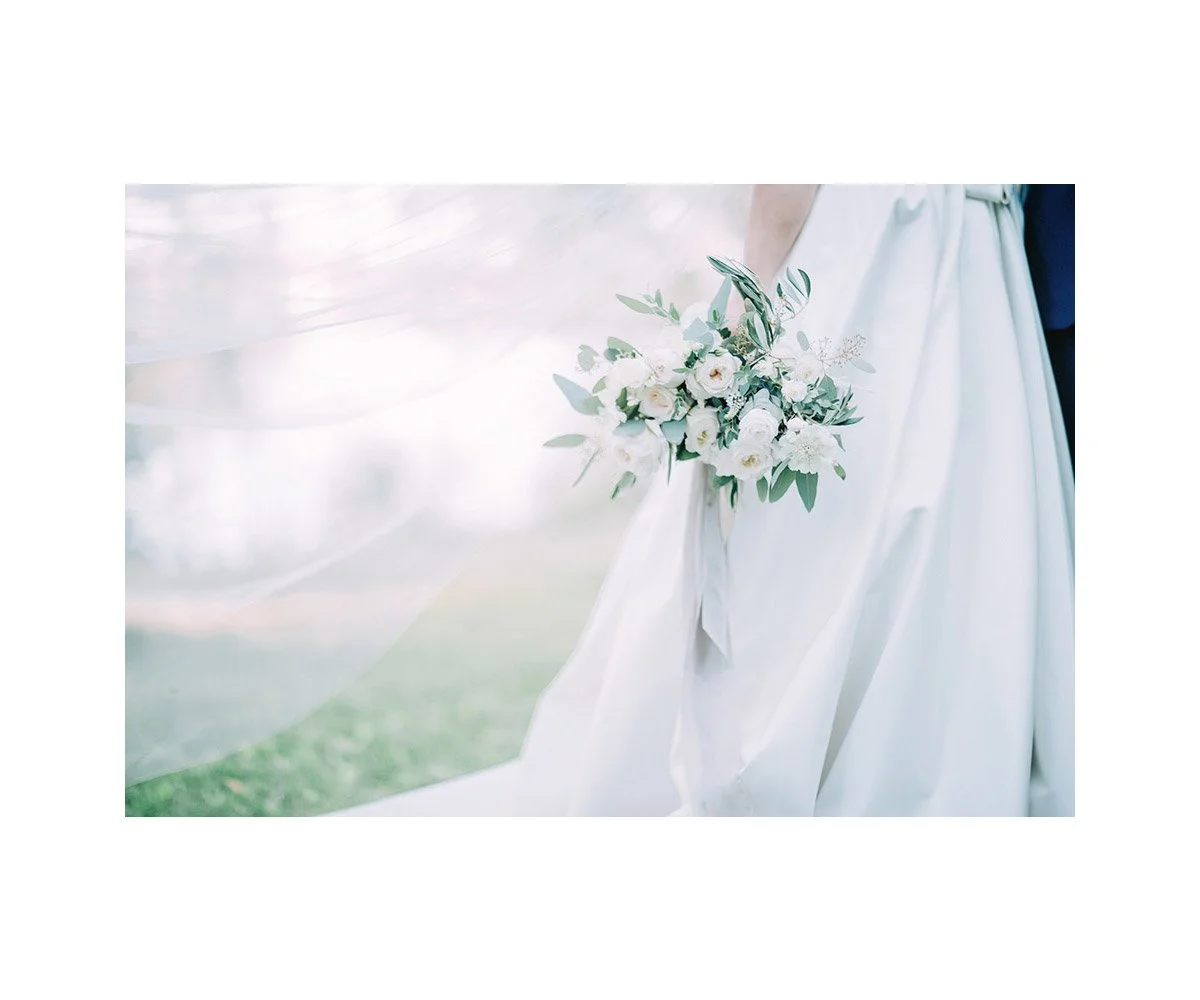 Wedding dress with a bouquet of white flowers and greenery, outdoors on a grassy area.