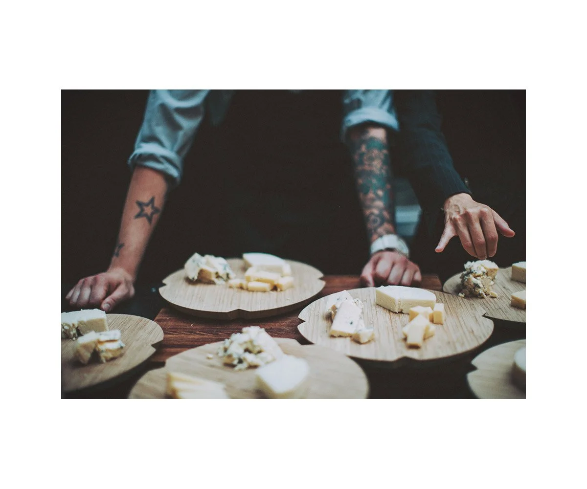 Person with tattoos reaching for cheese on wooden cheese boards.