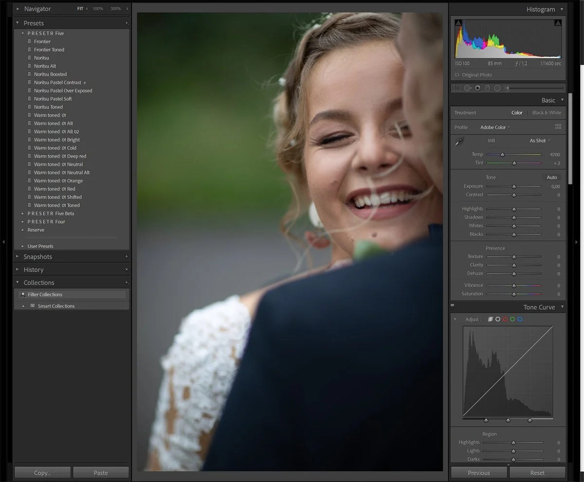 Close-up of a smiling woman with a wedding dress, embracing someone in a dark suit, outdoors with blurred green background.