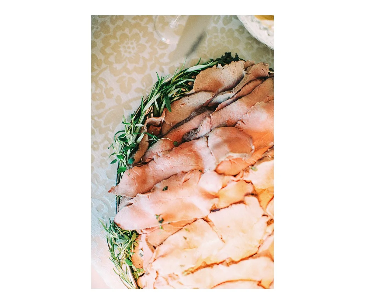 Close-up view of sliced smoked salmon garnished with fresh rosemary and herbs, laid out on a decorative tablecloth.