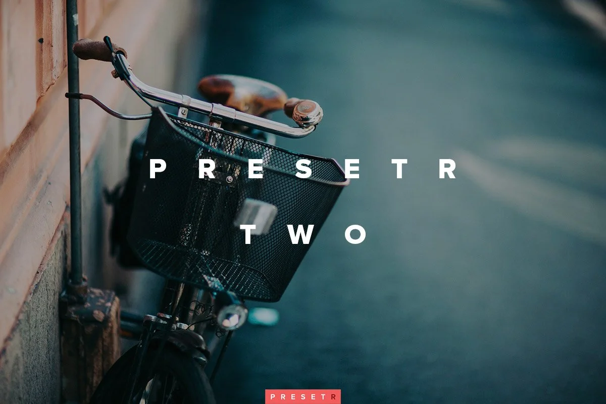 A black bicycle with a front basket leaning against a brick wall on a sidewalk with a blurred background