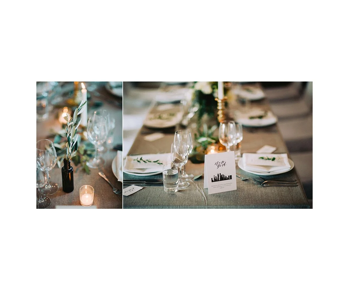 A decorated dinner table with candles, wine glasses, plates, napkins, and a small card with a city skyline silhouette, set for an event or celebration.