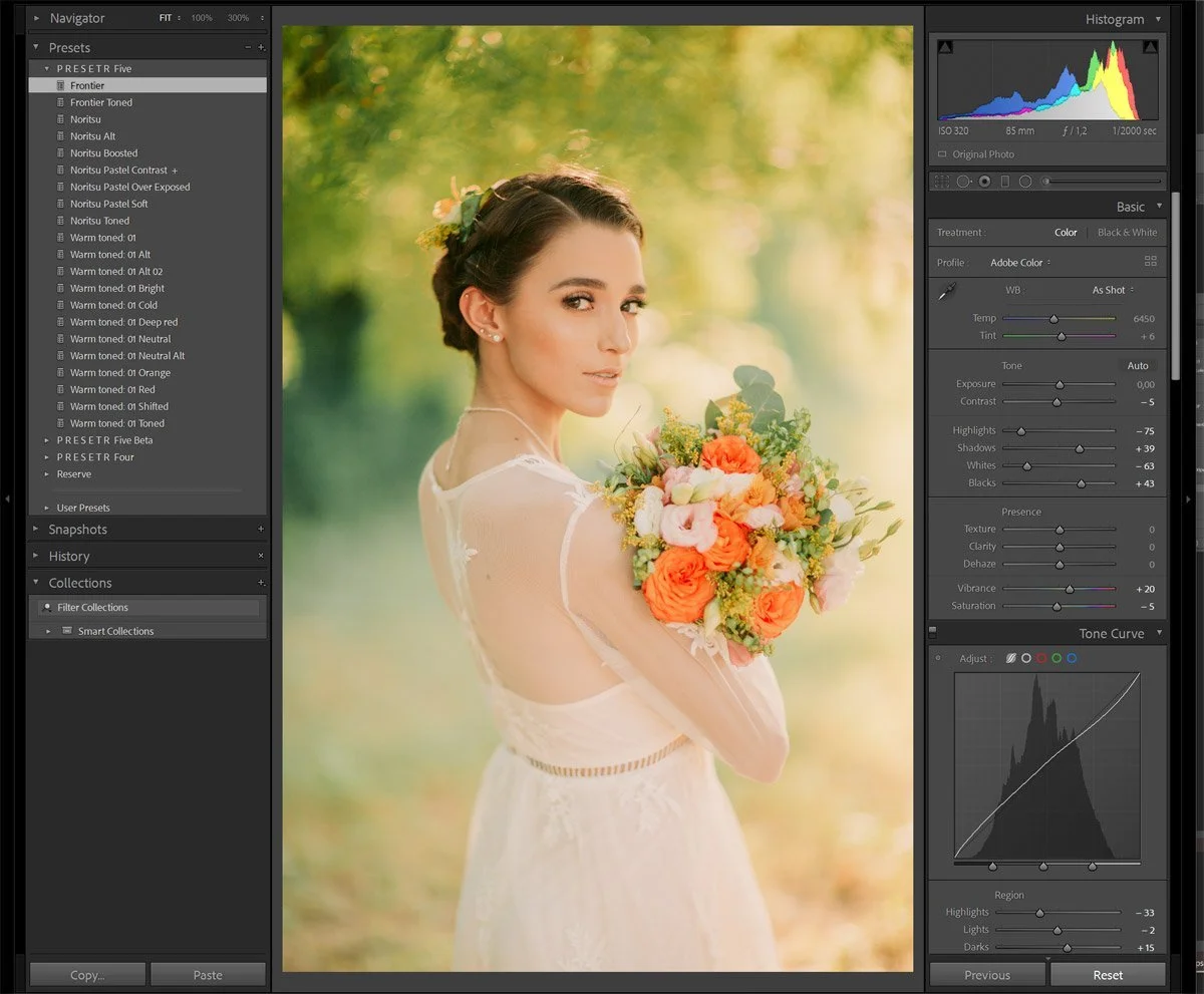A woman in a wedding dress holding a colorful bouquet of flowers outdoors, with a blurred green and yellow background.