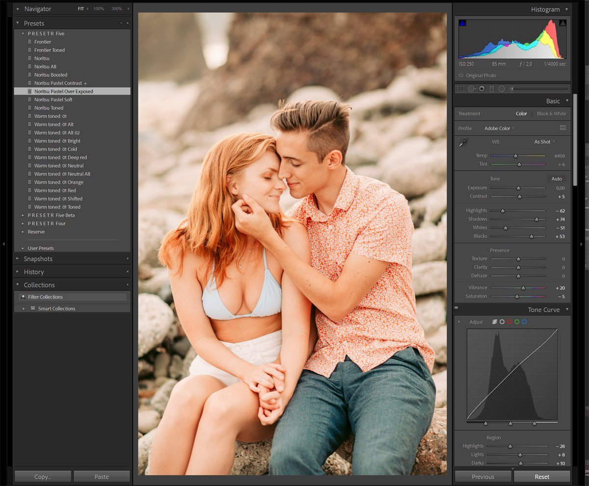 A young couple sitting on rocks outdoors, holding hands and leaning their foreheads together with eyes closed and smiling.