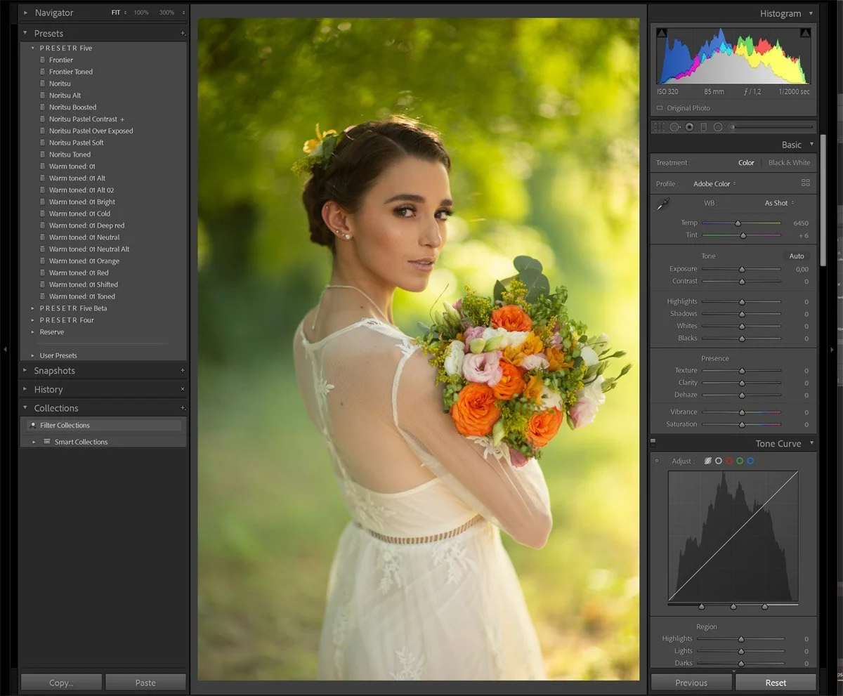 A woman in a white dress holding a colorful bouquet of flowers, outdoors with a green, blurred background and sunlight.