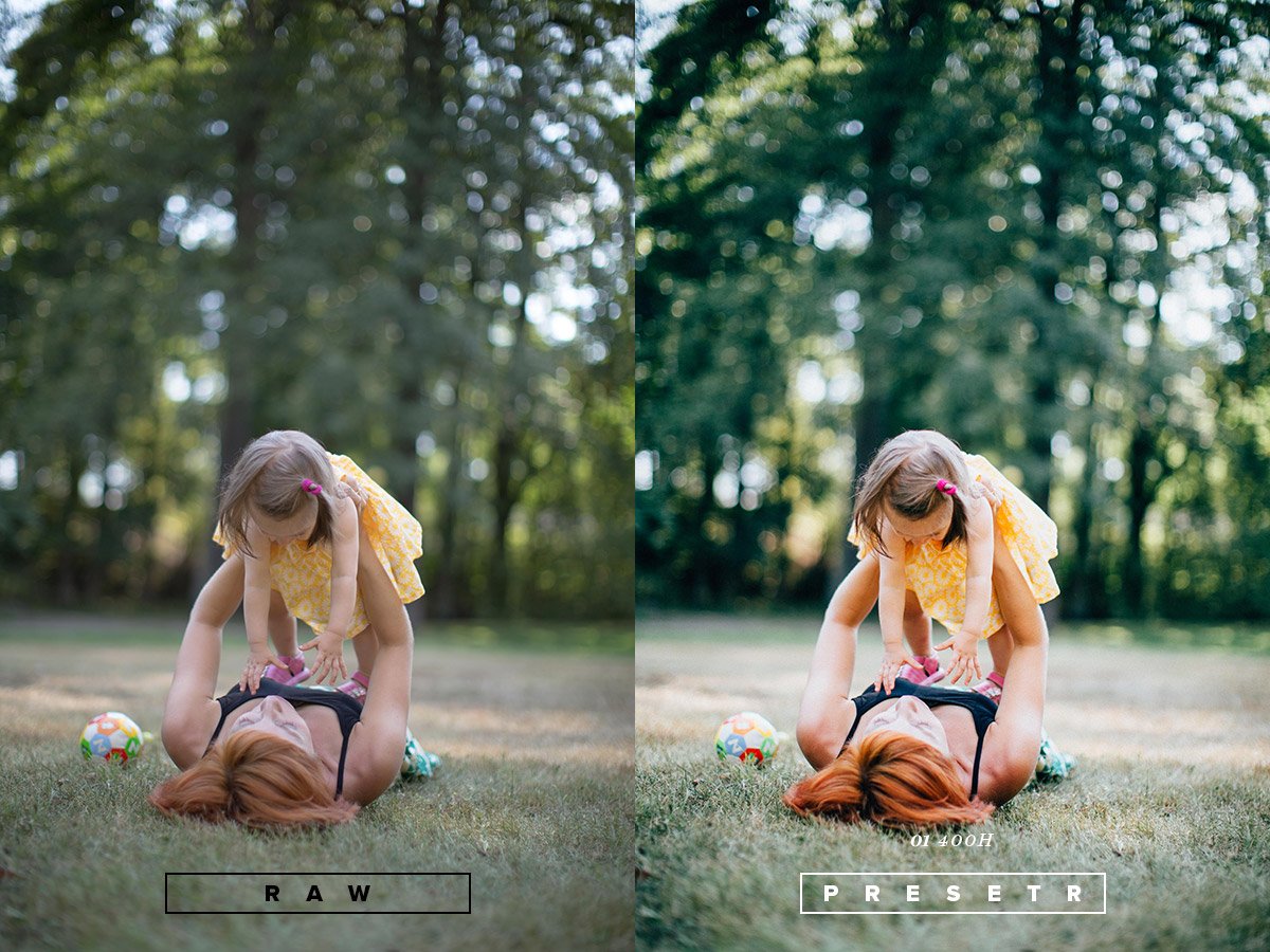 A woman with long reddish hair lying on the grass, lifting a young girl in a yellow dress with pink hair ties in an outdoor park setting. There are trees in the background, and a colorful ball is on the grass nearby.