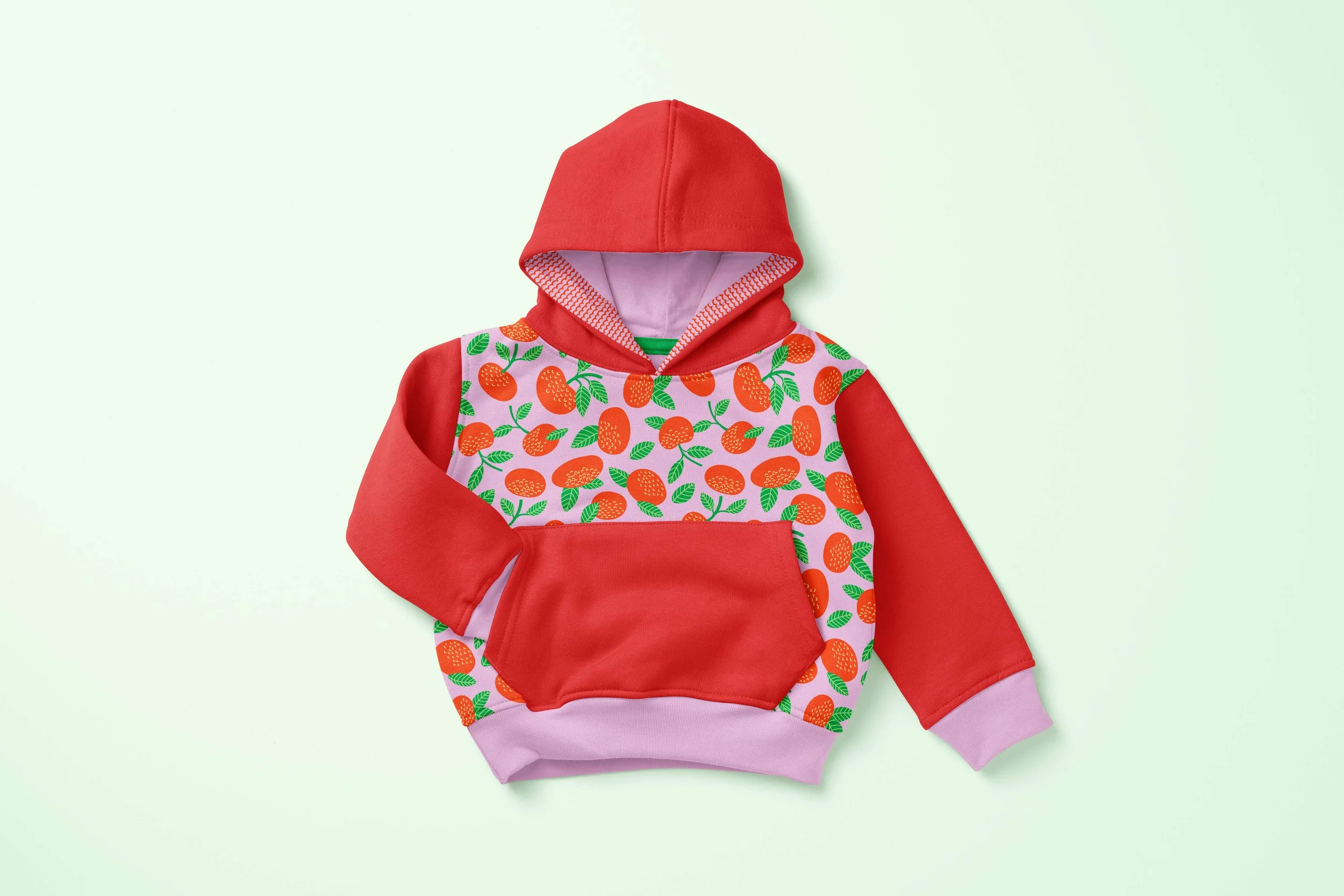 A color-blocked hoodie with red sleeves and hood, and pink trim. A citrus-fruit pattern on the main body section.
