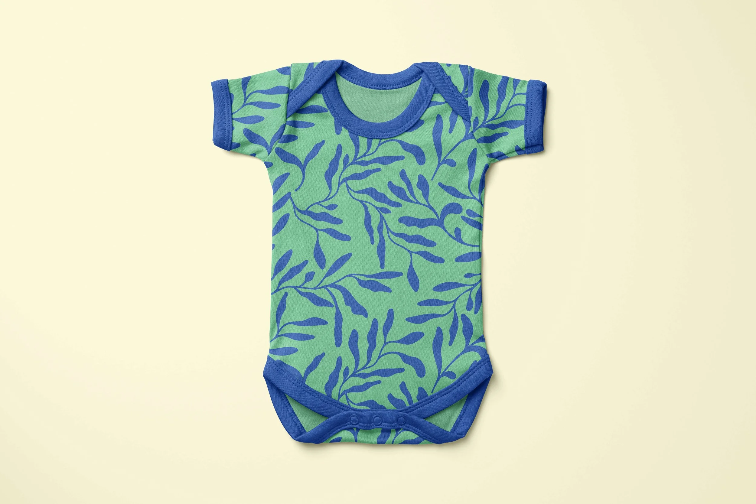 A short sleave onesie with a green and blue ocean botanical pattern that mimics kelp flowing in the water.