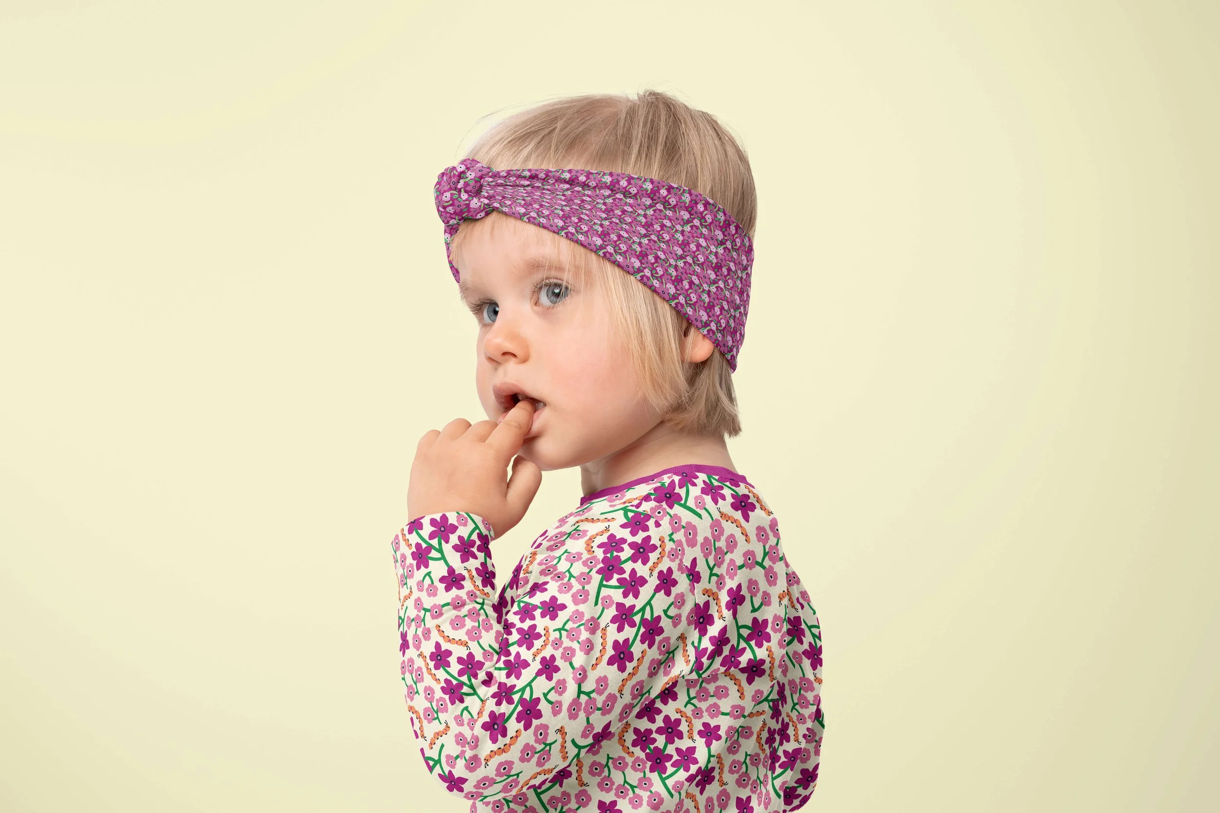 A little girl wearing a floral patterned headband and long-sleeve shirt featuring a pattern with flowers and cute caterpillars.