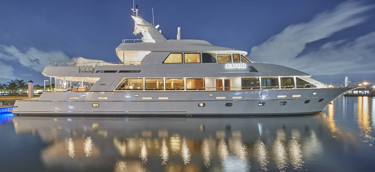 A large white yacht docked at a harbor during nighttime, with lights reflecting on the water.