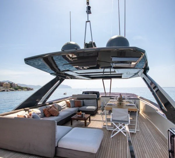 Luxury yacht with outdoor seating and dining area on deck, overlooking the ocean under a bright sky.