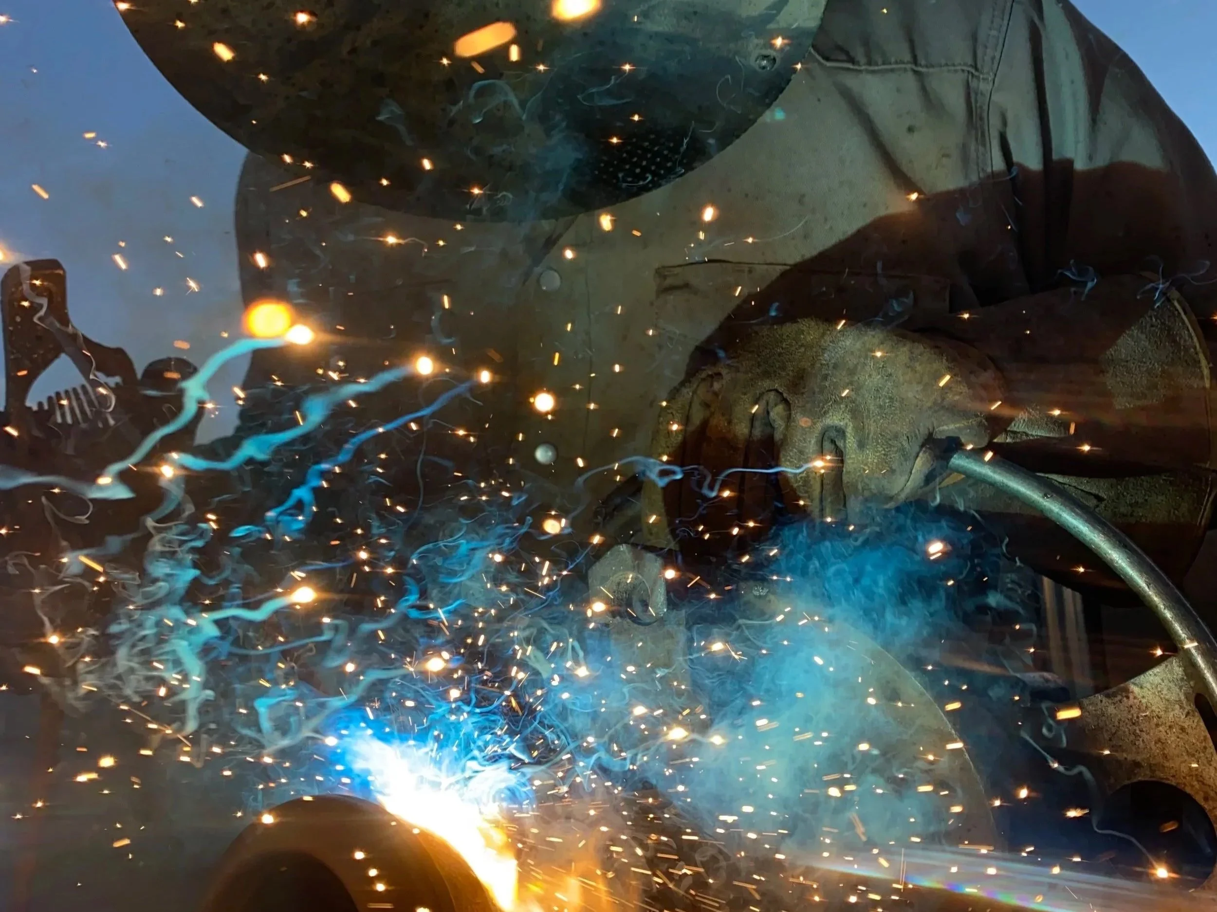 A person welding metal, with bright sparks and blue light from the welding process.