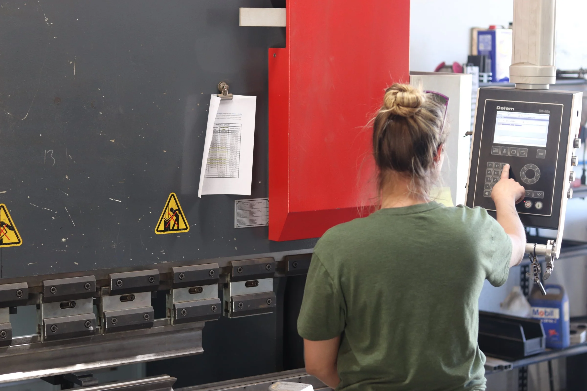 A woman with her hair in a bun operating industrial equipment with a control panel in a workshop or manufacturing environment.