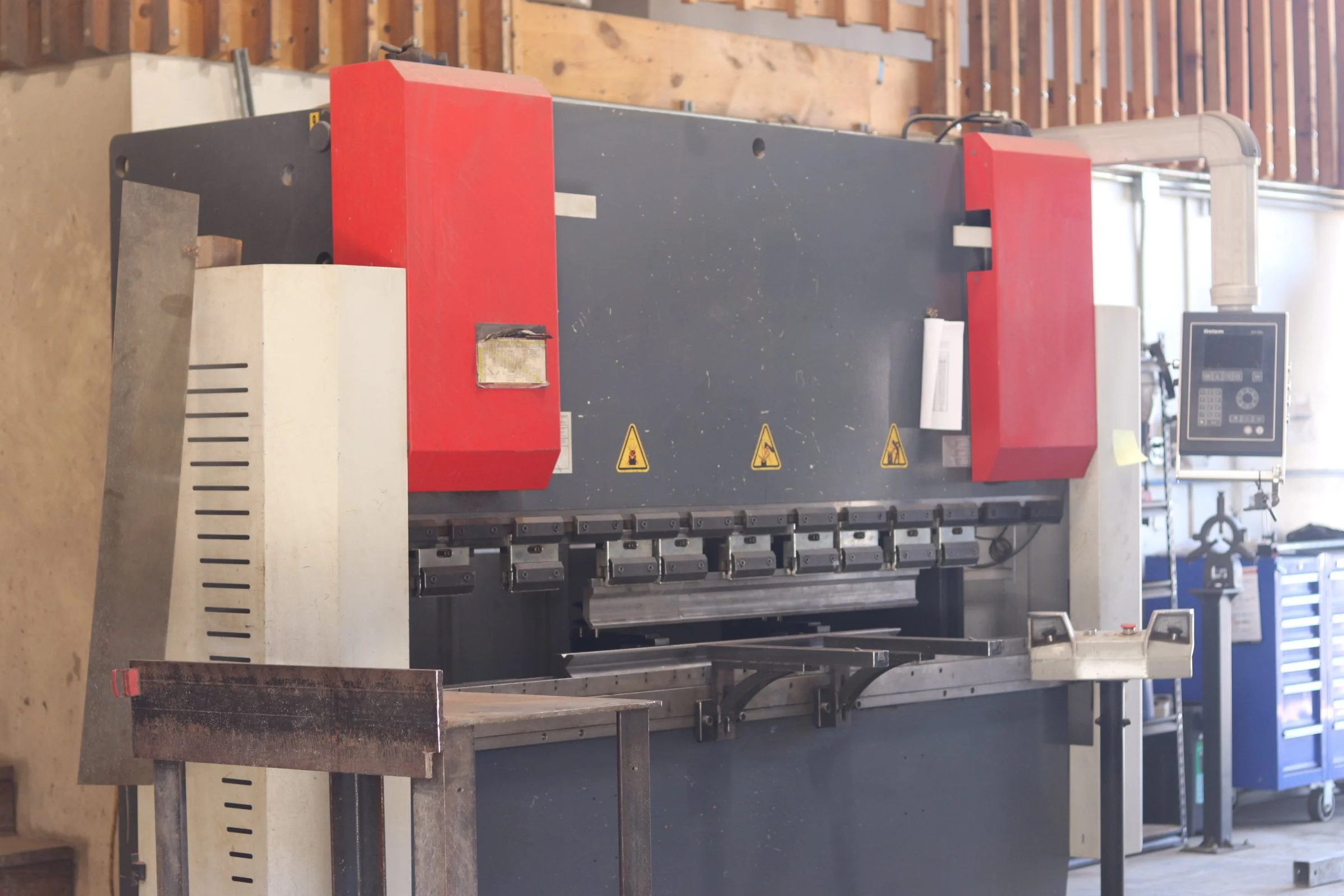 Press Break Industrial metal bending machine with warning signs in a workshop setting.