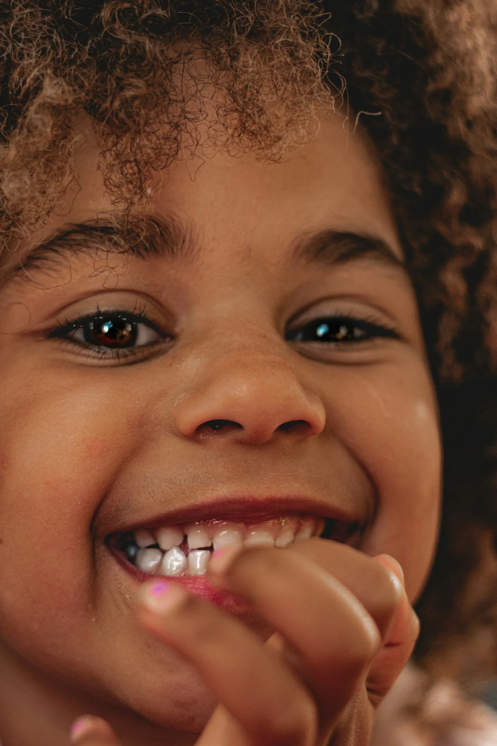 Close-up of a young girl with curly hair smiling and showing her teeth.