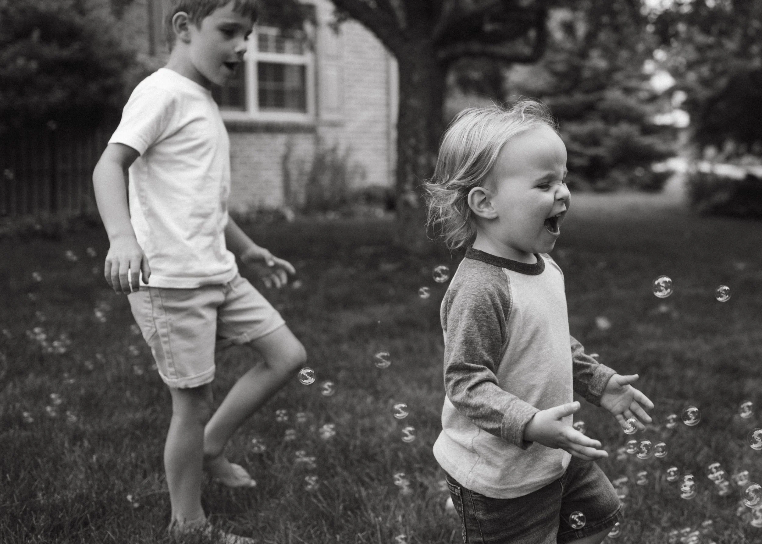 Two children playing outside with bubbles in a backyard, black and white photo.