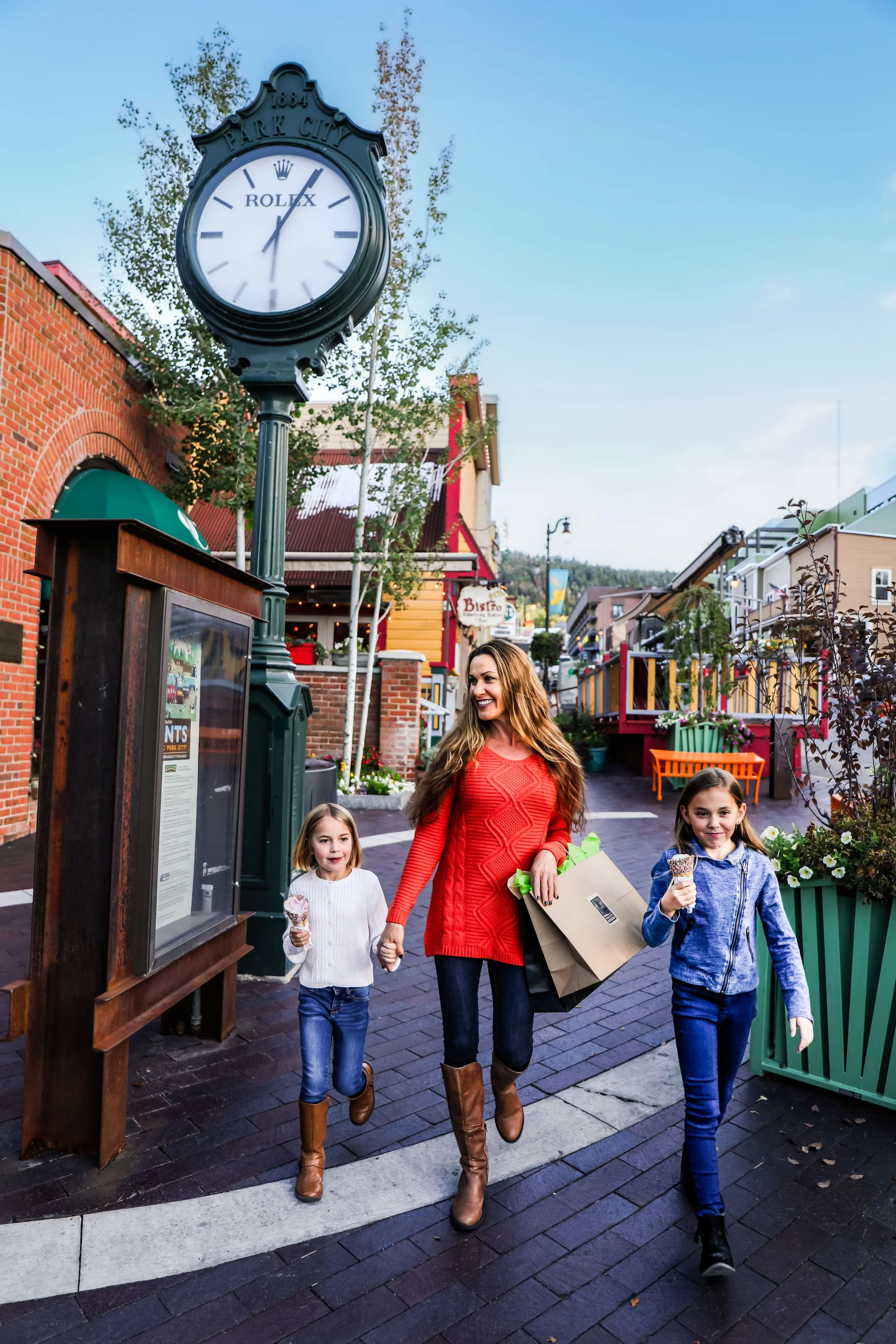 A woman and three children walking down a lively shopping street, with the woman holding shopping bags and the children eating ice cream.