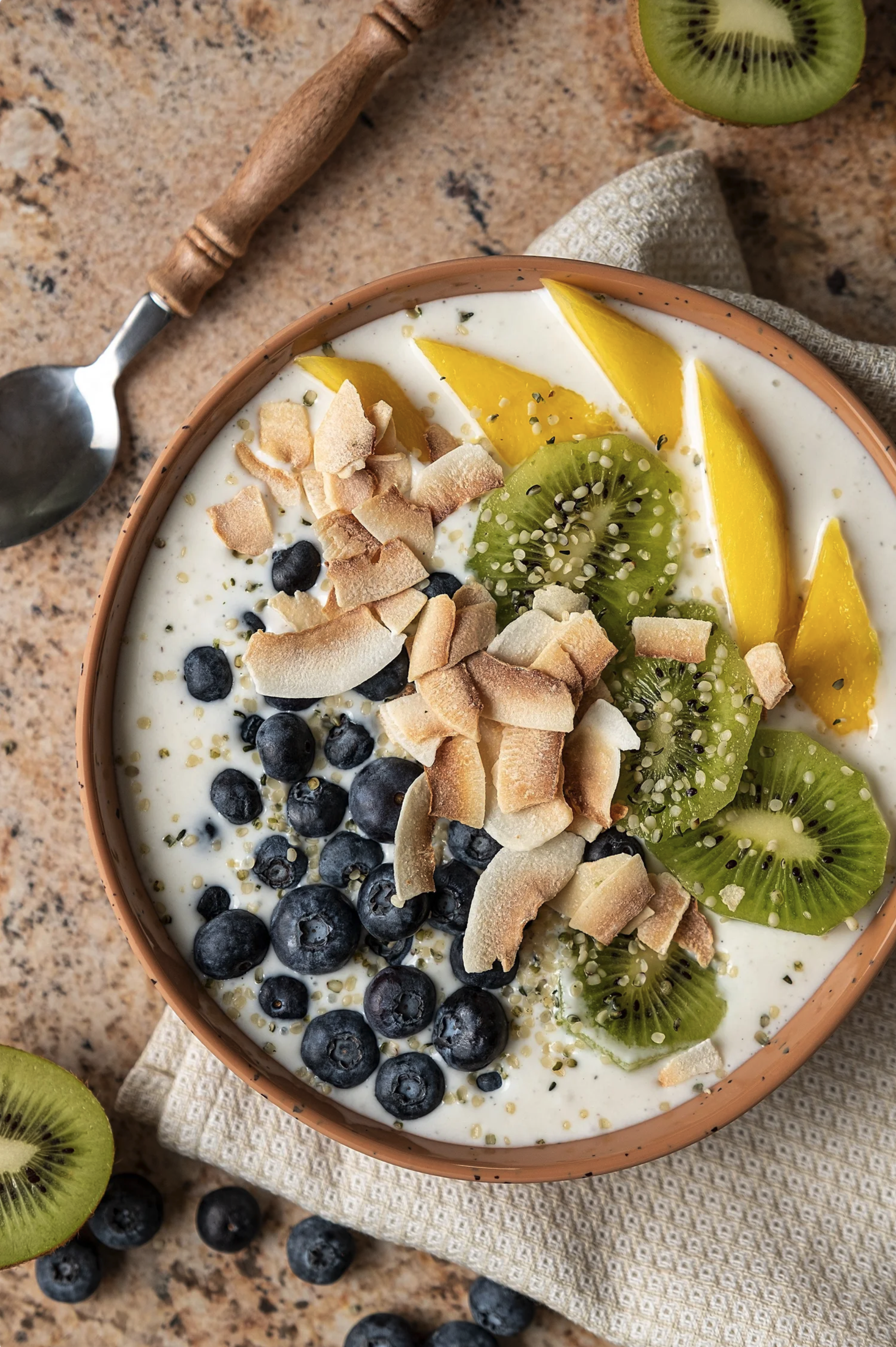 Bright morning smoothie bowl topped with sliced mango, kiwi, toasted coconut, and blueberries. Vibrant commercial food photography highlighting fresh ingredients for a healthy breakfast brand campaign.