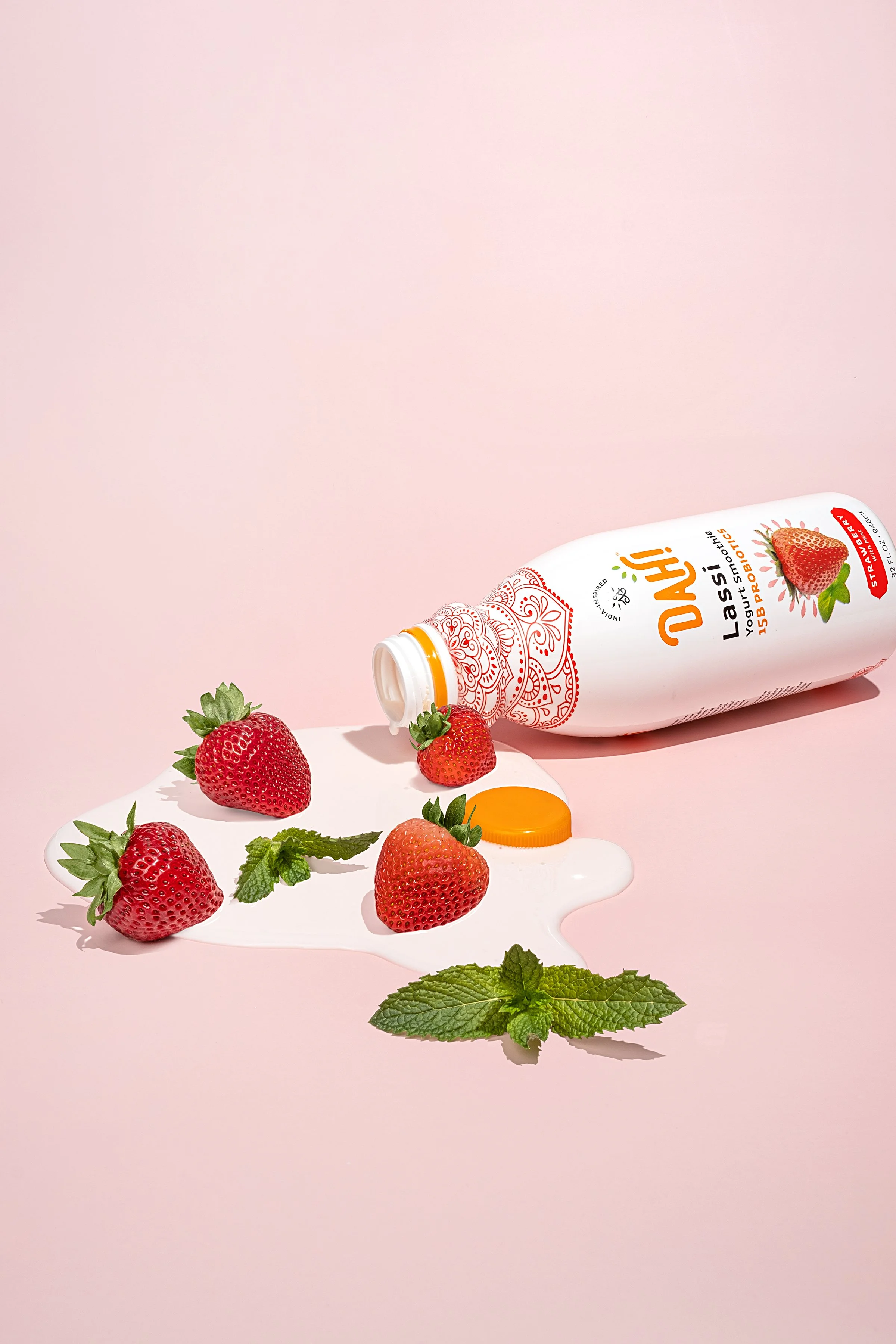Playful, graphic editorial product shot for a modern CPG wellness brand. Artistically composed on a colorful pink surface with a spilling beverage bottle, fresh fruit, and herbs for a high-contrast marketing campaign.