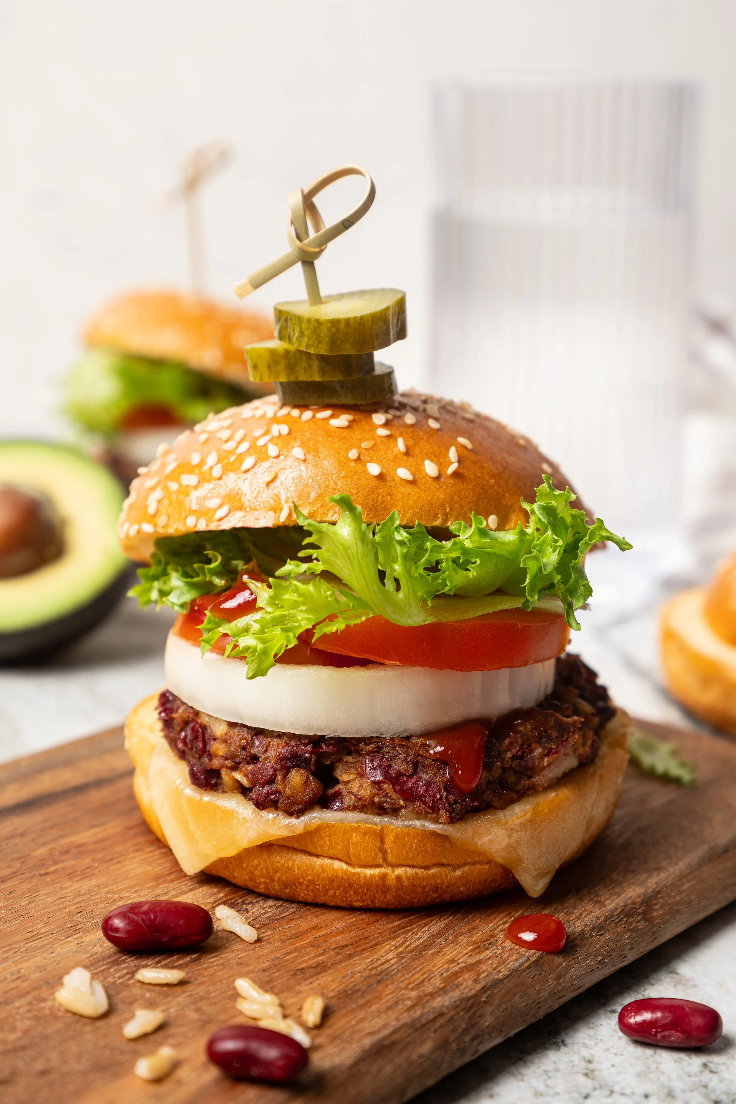 A towering homemade vegetarian bean burger on a wooden platter. Layered with cheese, onion, tomato, and lettuce on a sesame bun, featured as a healthy summer lunch recipe concept on the JodiLoves food blog.