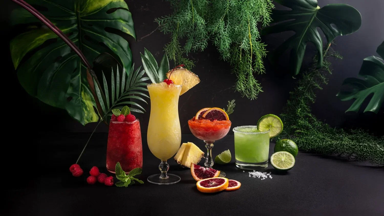 Commercial beverage photography for Ohio-based Nectar of the Vine and Julee Ho Media. A row of colorful tropical wine slushies styled with pineapple, lime, and blood orange against a dark background with lush tropical greenery.