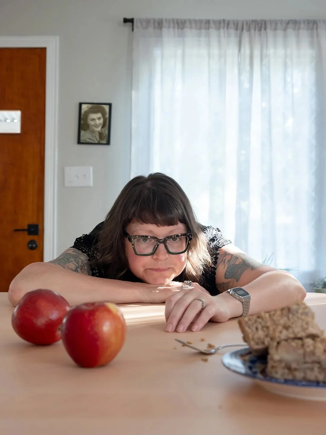 Editorial environmental portrait of a commercial food and still life photographer leaning on a table with fresh red apples and pastries, perfect for a creative studio homepage introduction.