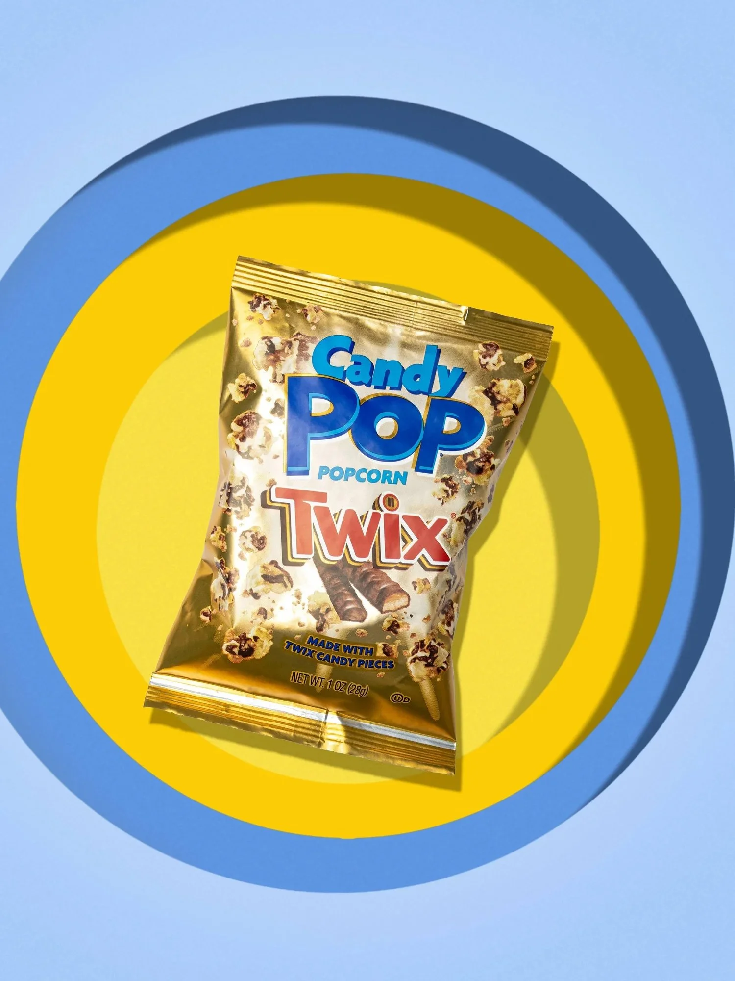 Commercial product photography for Candy Pop and agency The Anton Eye. A gold popcorn snack bag is centered on a vibrant yellow and blue layered circular background under bright studio lighting.