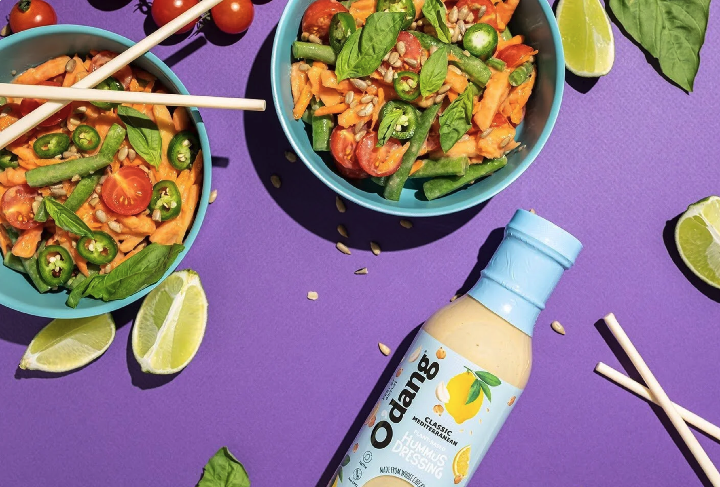 Commercial food photography for O'dang Hummus Dressing and agency The Anton Eye. A flat lay of a spicy Mediterranean salad in teal bowls with fresh limes and jalapenos on a vibrant purple background.