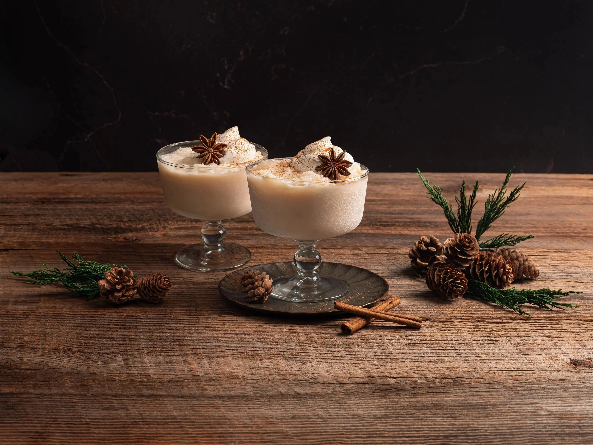 Editorial photograph of a spiced winter wine slushy cocktail. Beautifully styled from an eye-level view with whole star anise, rustic cinnamon sticks, and pinecones on a cabin wood table for a seasonal marketing campaign.