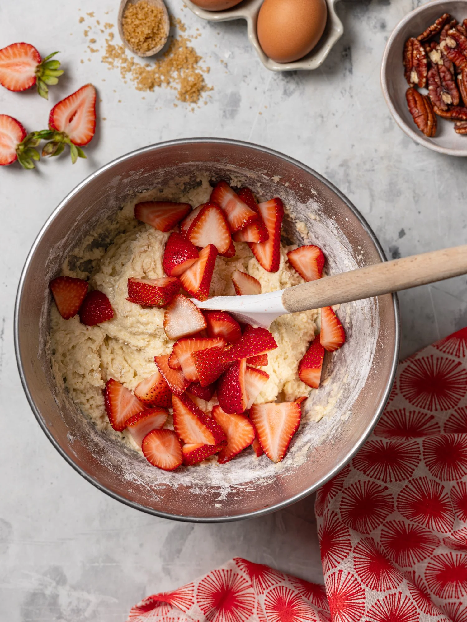 Step-by-step baking process shot for a strawberry coffee cake recipe on the JodiLoves blog. Sliced red strawberries are piled into thick cake batter inside a stainless steel stand mixer bowl, ready to fold with a spatula.