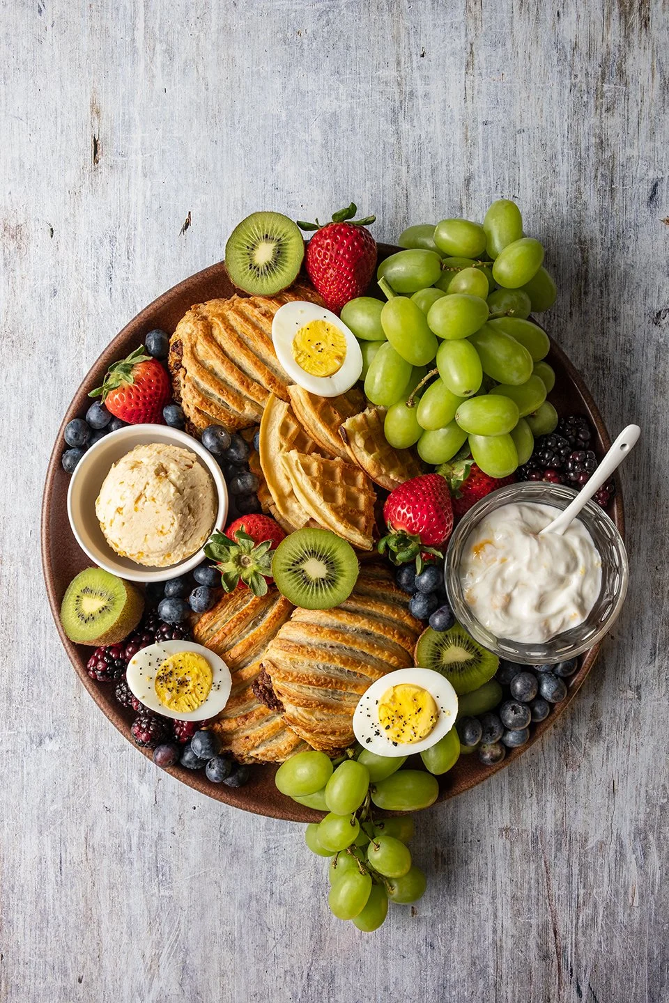 Overhead food photography for Wise Butter. An artisanal breakfast platter featuring fresh pastries, fruit, and a jar of premium peach butter, beautifully styled on a neutral surface for a commercial brand campaign.