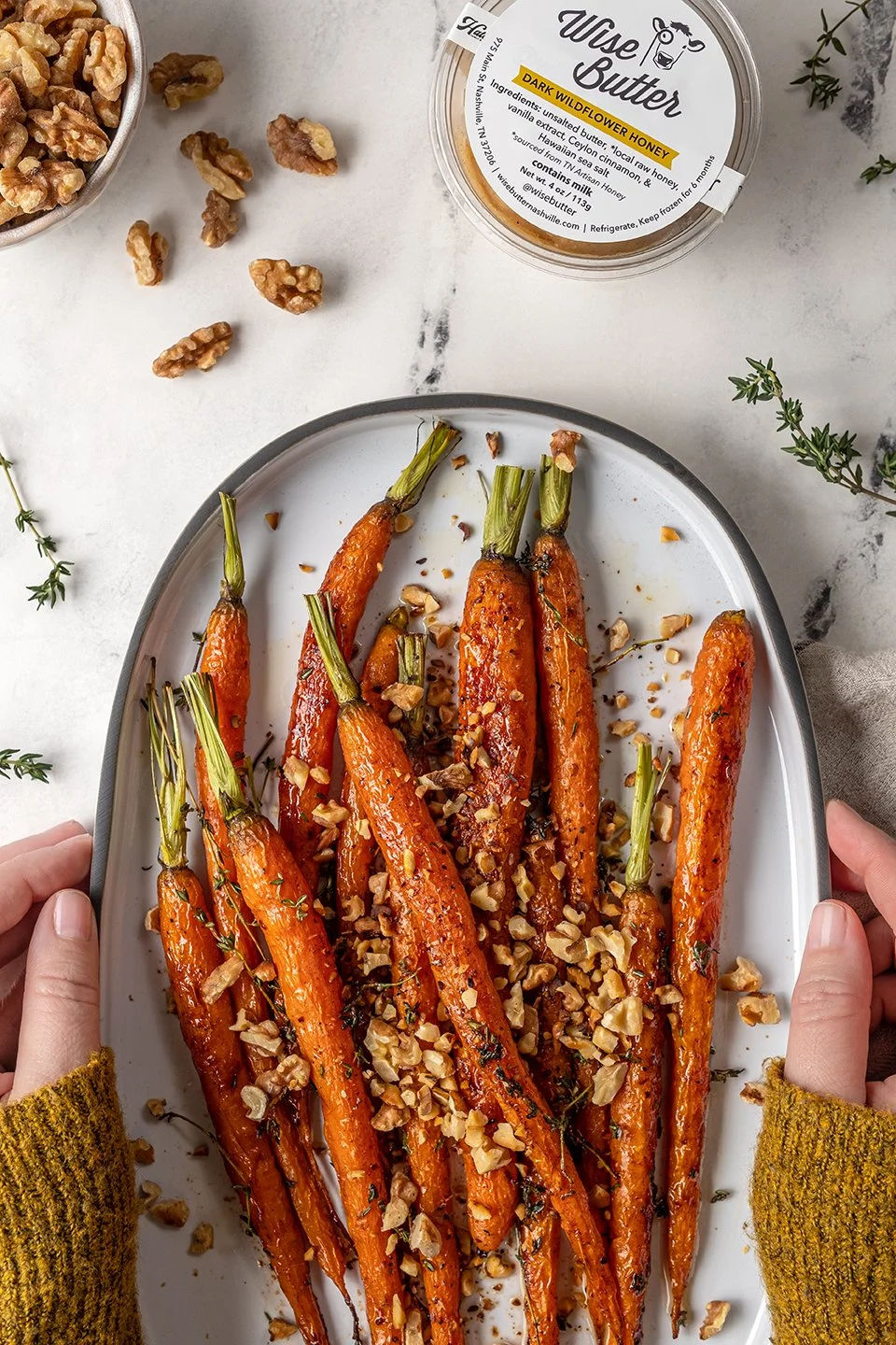 Commercial food photography for Wise Butter. Artistically styled roasted carrots topped with chopped walnuts and a pat of premium butter, featuring warm tones and cozy vibes for a brand campaign.