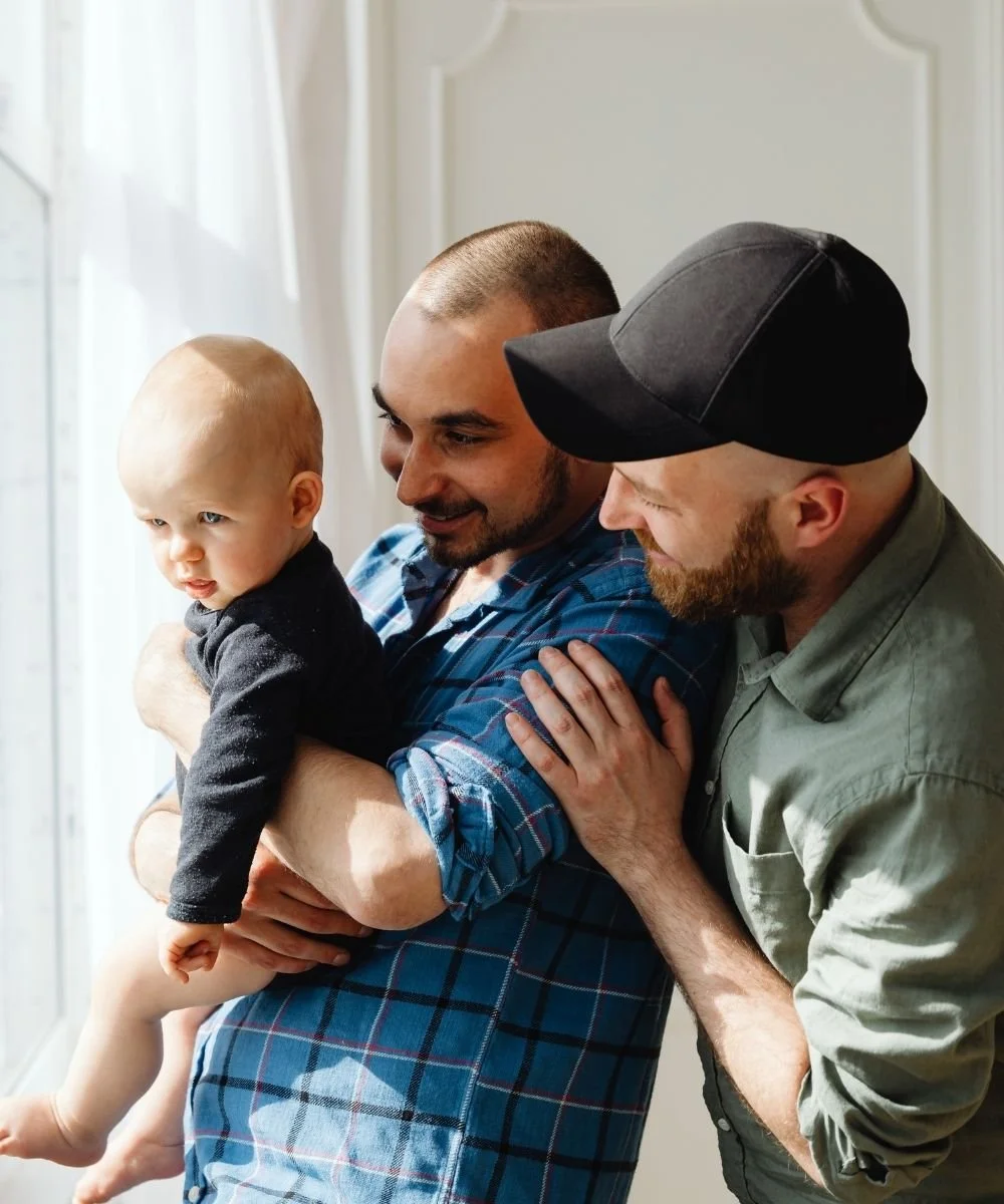 Male couple holding their child looking out the window