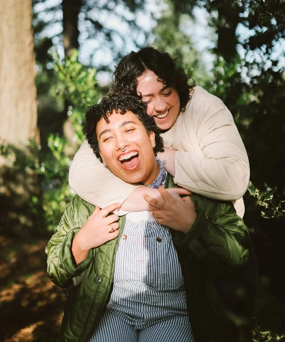 Non-binary person and their friend hugging and laughing