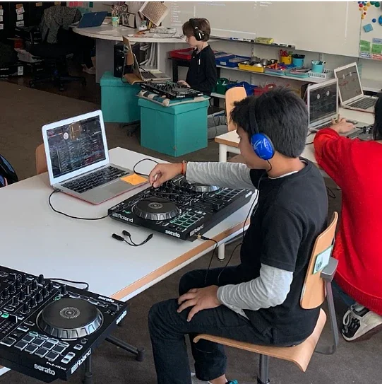 Students working at DJ controllers and laptops in a classroom