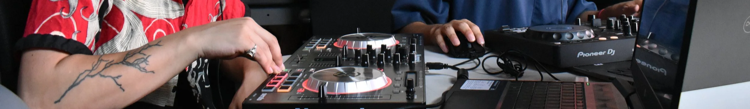 People using DJ equipment, including a controller, laptop, and monitor, during a music session.